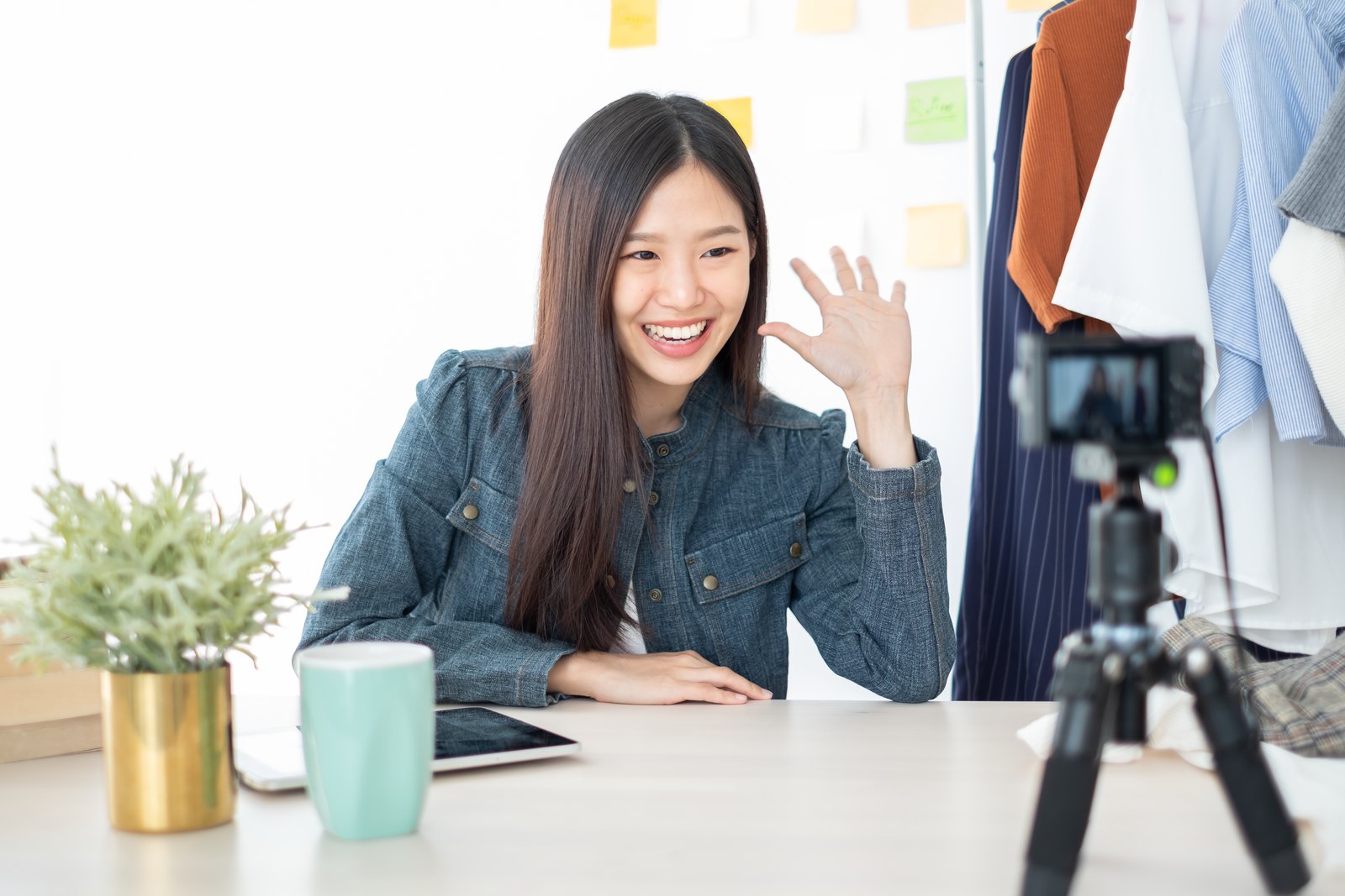 Content creator waving to a camera while recording at her desk